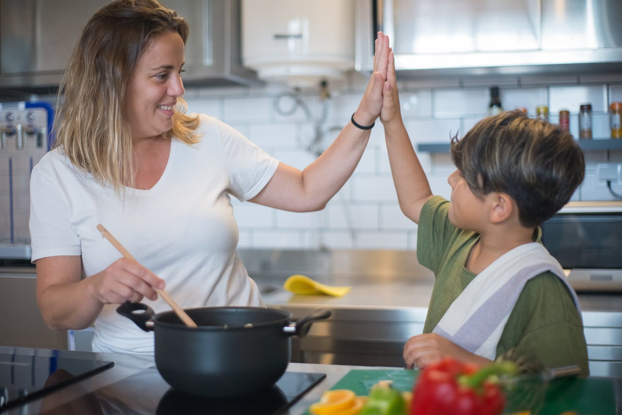 A mother and son share a high five while cooking together in a modern kitchen.
